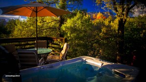 Un bain à remous avec une terrasse en bois et un parasol, entouré d’arbres et offrant une vue sur la montagne.