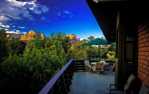 A deck with outdoor furniture, a table, and an umbrella, overlooking a forest and mountains.