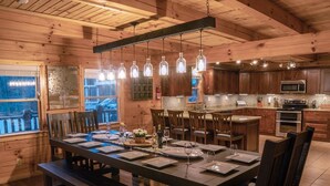 A wooden interior with a dining table set for six, kitchen cabinets, a microwave, and a stove. - The Lodge: Sleeps 23 - Hot Tub, Fire Pit, Game Room (Logan)