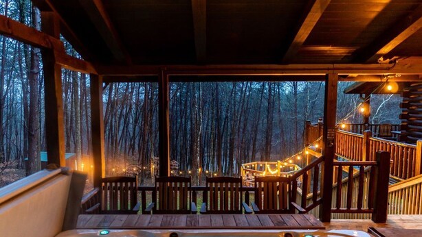 A hot tub area with wooden deck seating and a view of a forested area. - The Lodge: Sleeps 23 - Hot Tub, Fire Pit, Game Room (Logan)