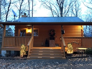 A log cabin with a porch, a wreath on the wall, and two lit Christmas trees. - MountainView Cutest Bear Cabin in Gatlinburg Cozy Close to Town Hot Tub Romantic (Gatlinburg)