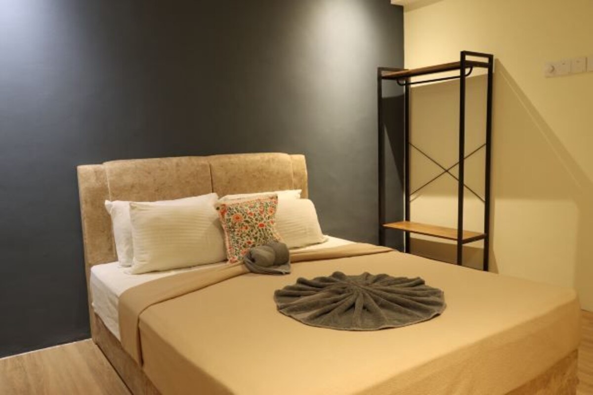 A bedroom with a bed, pillows, a blanket, a small shelf, and a wall-mounted rack.