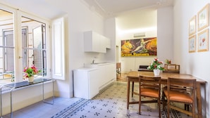 A compact kitchen with white cabinets, a sink, and a dining area with a wooden table and chairs. - Rental In Rome Arenula Apartment (Rome)