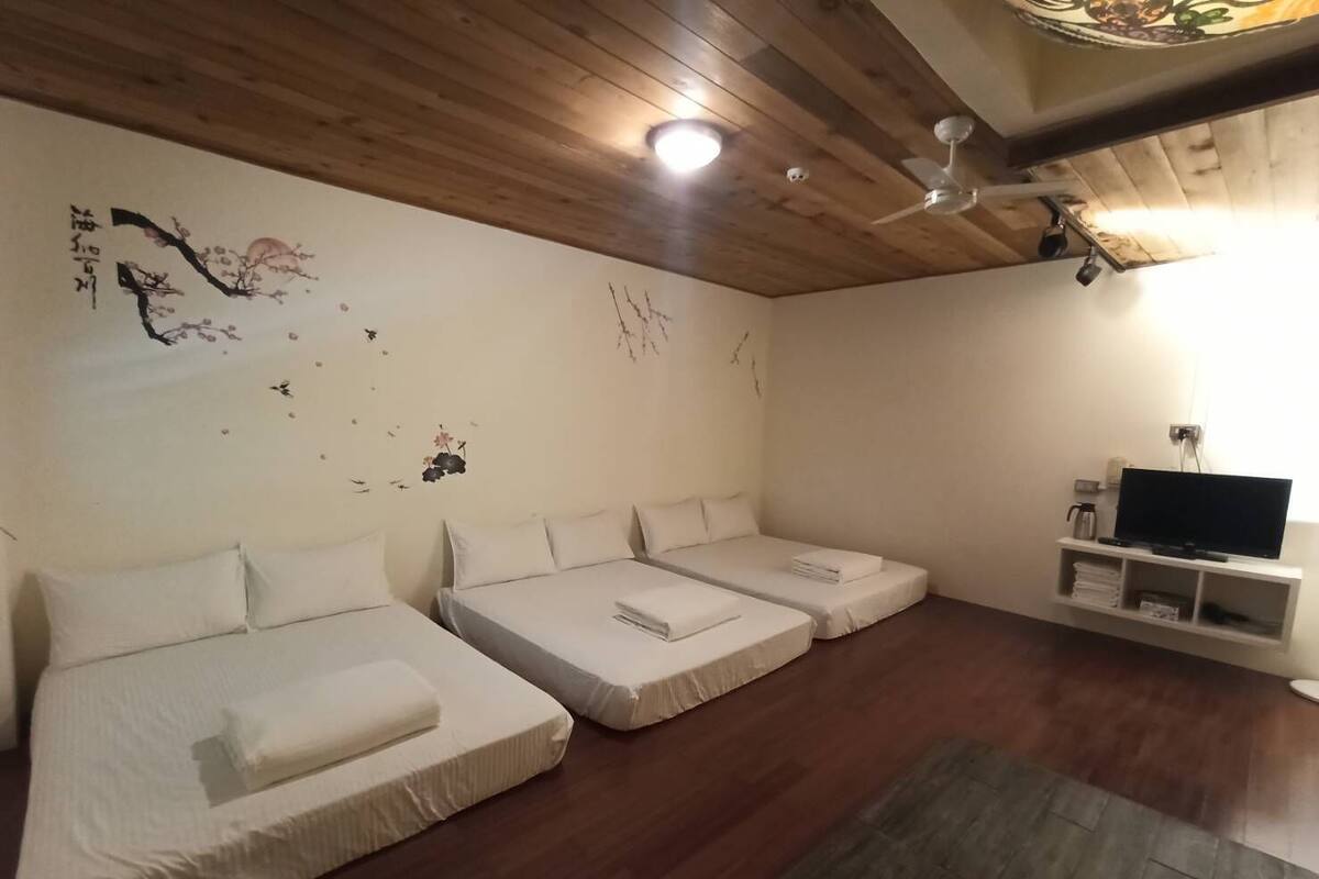 Habitació d'hotel amb tres llits, televisió i ventilador de sostre.