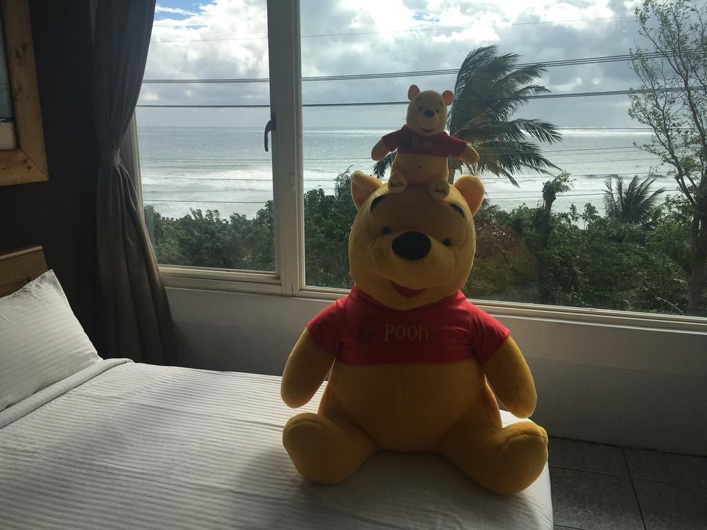 A plush Winnie the Pooh toy on a bed with a view of the ocean through a window.