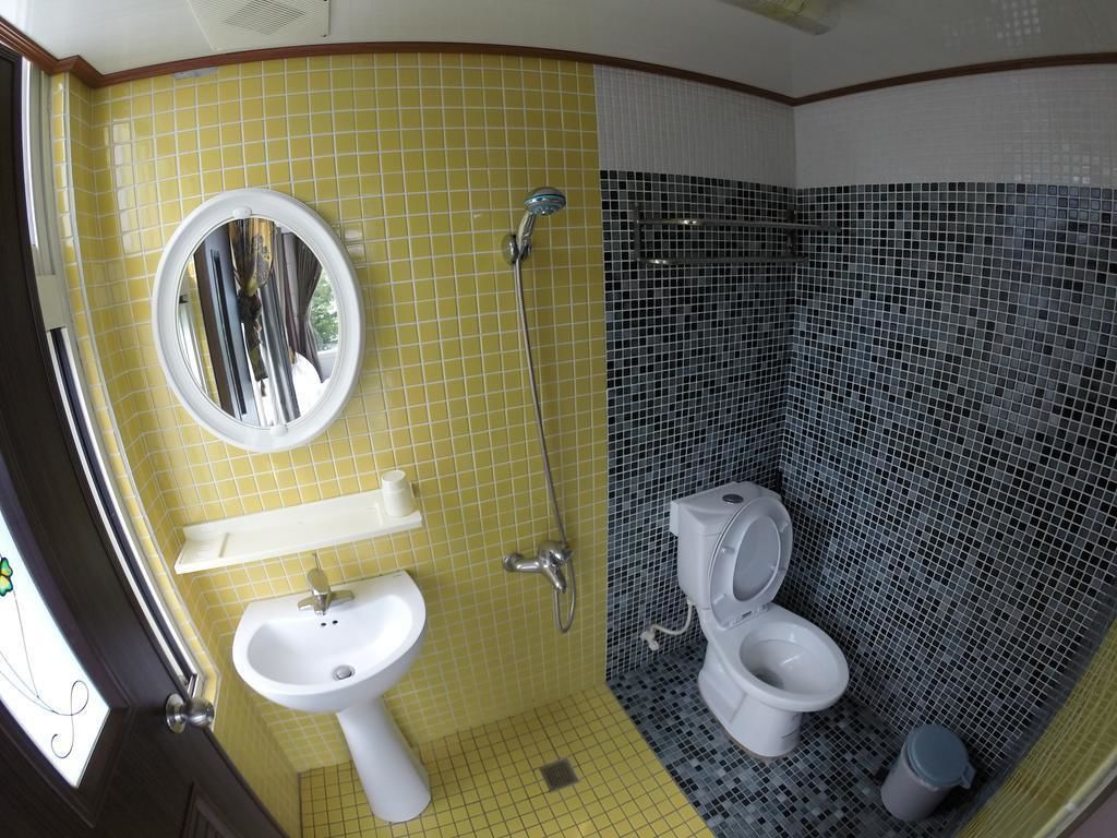 Un baño con pared de azulejos amarillos, un lavabo blanco, un espejo, una ducha y un inodoro.