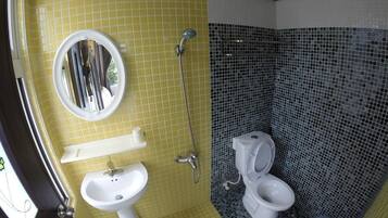 Un baño con pared de azulejos amarillos, un lavabo blanco, un espejo, una ducha y un inodoro.