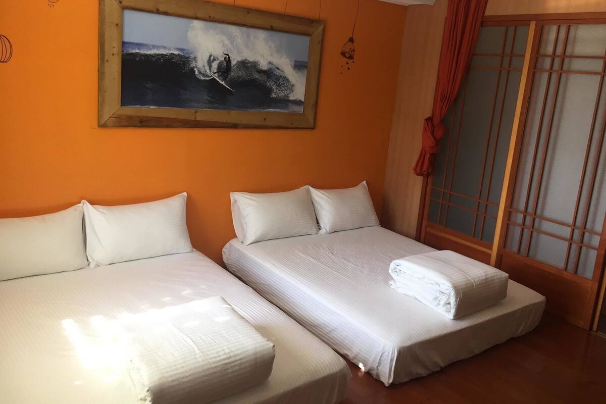 Habitació amb dos llits, un quadre d'un surfista i una porta corredissa amb cortines vermelles.
