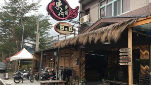 Un restaurant doté d’une terrasse, d’un toit de chaume et d’une enseigne arborant le logo d’un établissement proposant à la fois des chambres et des repas.