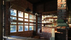 Un coin bar au style rustique, avec des murs en briques, de grandes fenêtres et une pancarte indiquant « Bienvenue ».
