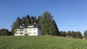 A two-story house with a sloped roof, surrounded by a grassy field and dense trees. - Mountain idyll in the Steigerhaus Sauerland - DG Nord (Andreasberg)