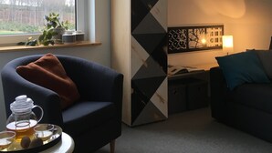 A modern living room with a sofa, a coffee table with a tea set, a tall cabinet with geometric patterns, and a view of trees through a window. - Mountain idyll in the Steigerhaus Sauerland - DG Nord (Andreasberg)
