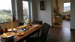 Un comedor con una mesa de madera dispuesta para una comida, una araña y vistas a un jardín a través de amplios ventanales.