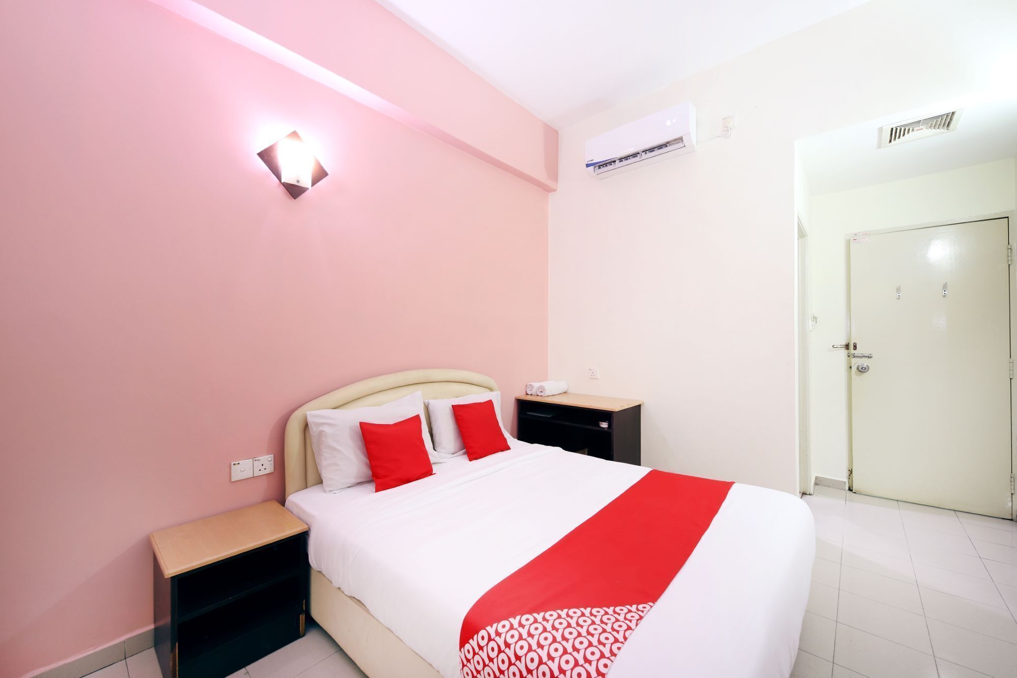 A hotel room with a bed, bedside tables, a nightstand, a wall-mounted air conditioner, and a door.