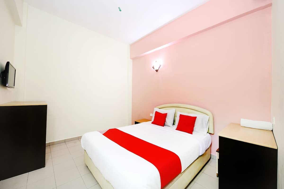Ein Hotelzimmer mit Bett, Nachttisch, Wand-Fernseher und Lampe über dem Bett.