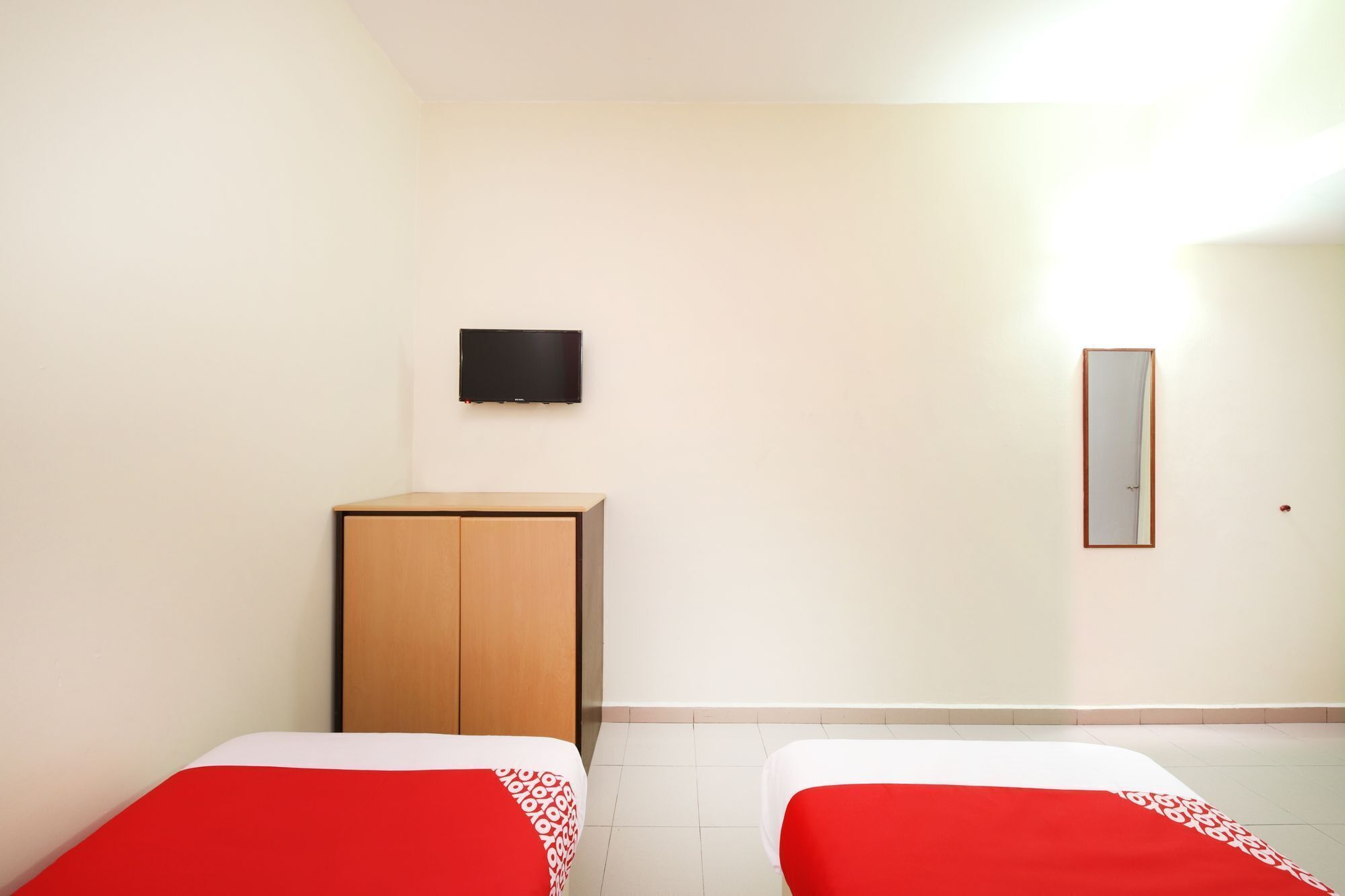 A hotel room with two beds, a television on the wall, and a mirror.