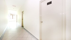 Un pasillo con una puerta blanca con el número 25 y una puerta al final con ventanal.