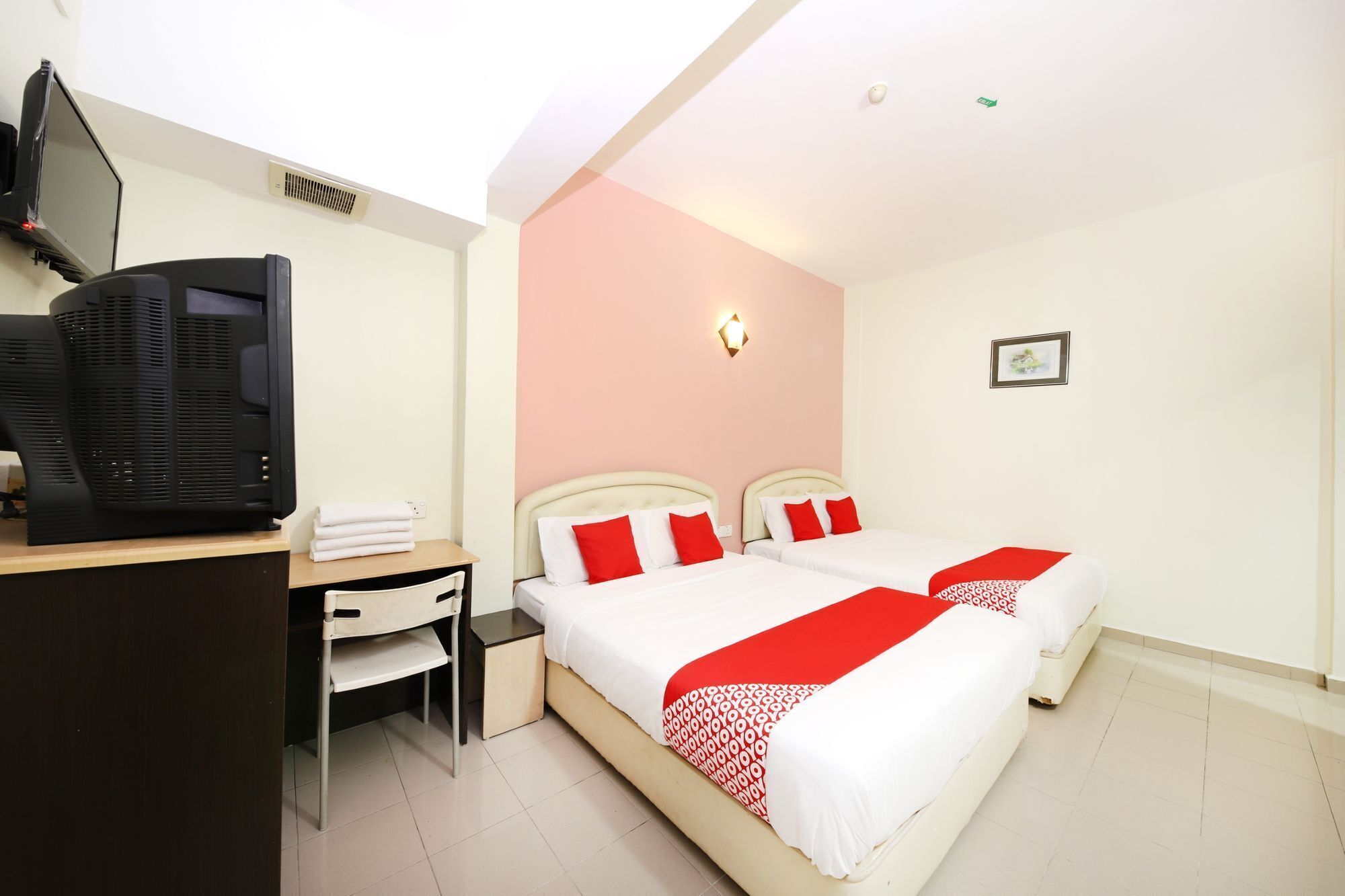 A hotel room with two beds, a desk, a television, and a small bedside table.