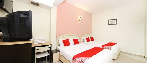 A hotel room with two beds, a desk, a television, and a small bedside table.