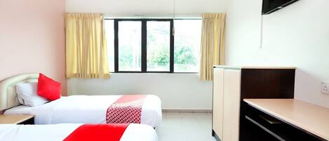 A hotel room with two beds, a desk, a TV, and a window with curtains.