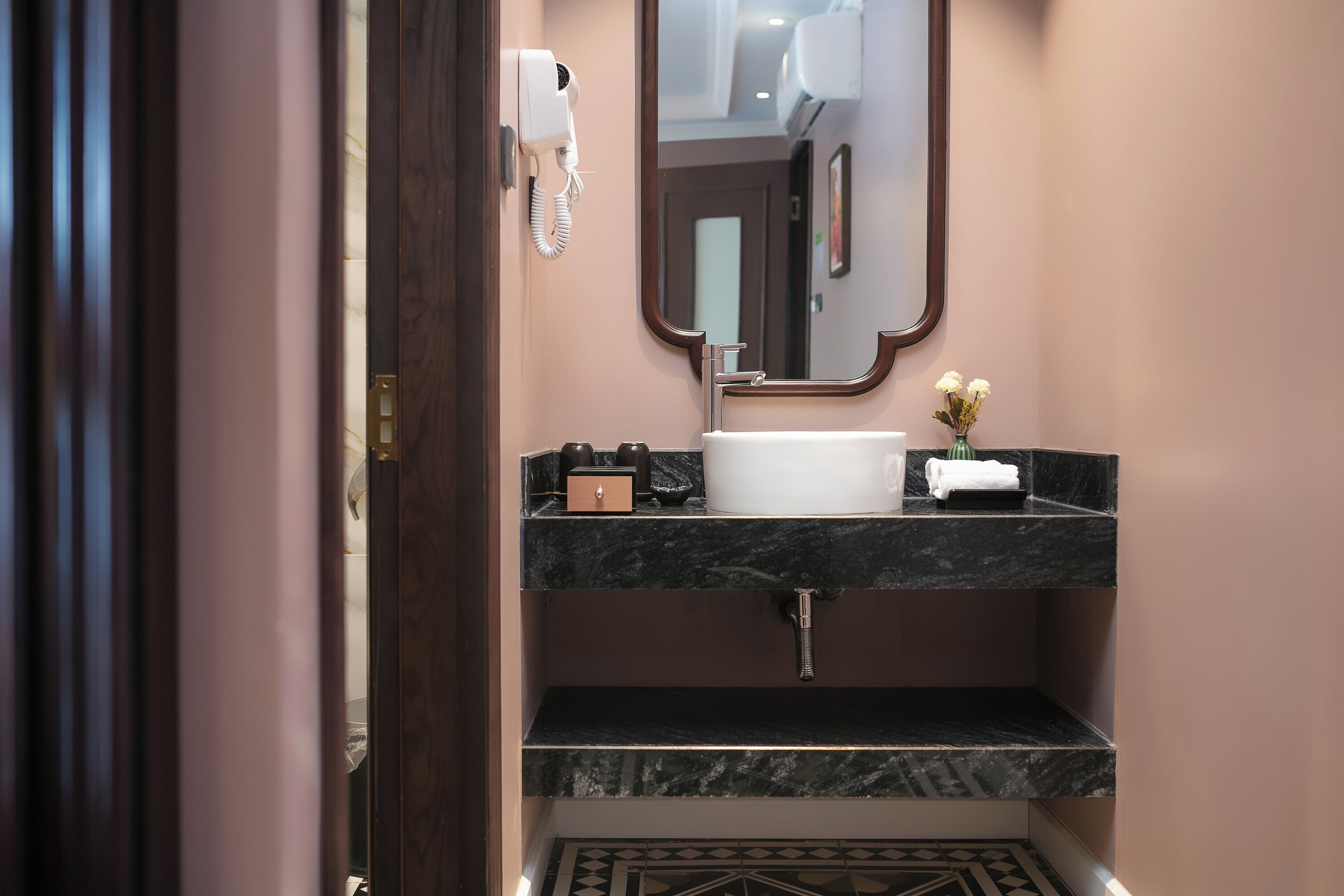 Un bagno con lavabo in marmo, uno specchio, un asciugacapelli e un vaso con fiori.