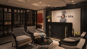 A reception area with a modern design, featuring a reception desk, two armchairs, a small round table with a vase of flowers, and a decorative wall with the logo "INDO SPA". - Acoustic Hotel & Spa (Hanoi)