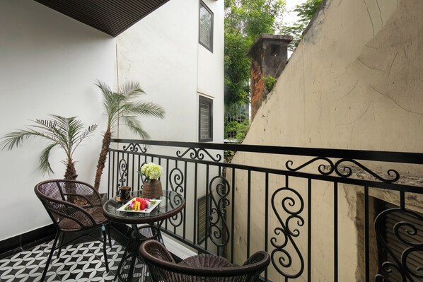 Un balcon doté d’un sol carrelé en noir et blanc, de deux fauteuils en osier, d’une petite table ronde ornée d’un vase de fleurs et d’une plante en pot.