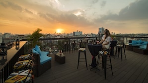 A rooftop terrace with outdoor seating, a bar area, and a city skyline view at sunset. - Acoustic Hotel & Spa (Hanoi)