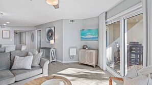 A modern living room with a grey sofa, a wooden coffee table, and a large window with a view of outdoor furniture. - ***DIRECT GULF VIEWS**FREE UMBRELLA SERVICE**PET FRIENDLY**UPSCALE CONDO** (Miramar Beach)