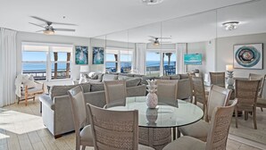 A spacious living room with a round glass table, comfortable seating, and large windows offering a view of the ocean. - ***DIRECT GULF VIEWS**FREE UMBRELLA SERVICE**PET FRIENDLY**UPSCALE CONDO** (Miramar Beach)
