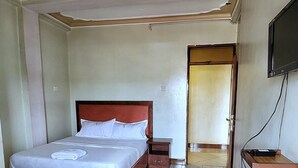 Ein Hotelzimmer mit Bett, Holzstuhl, kleinem Tisch und Fernseher.