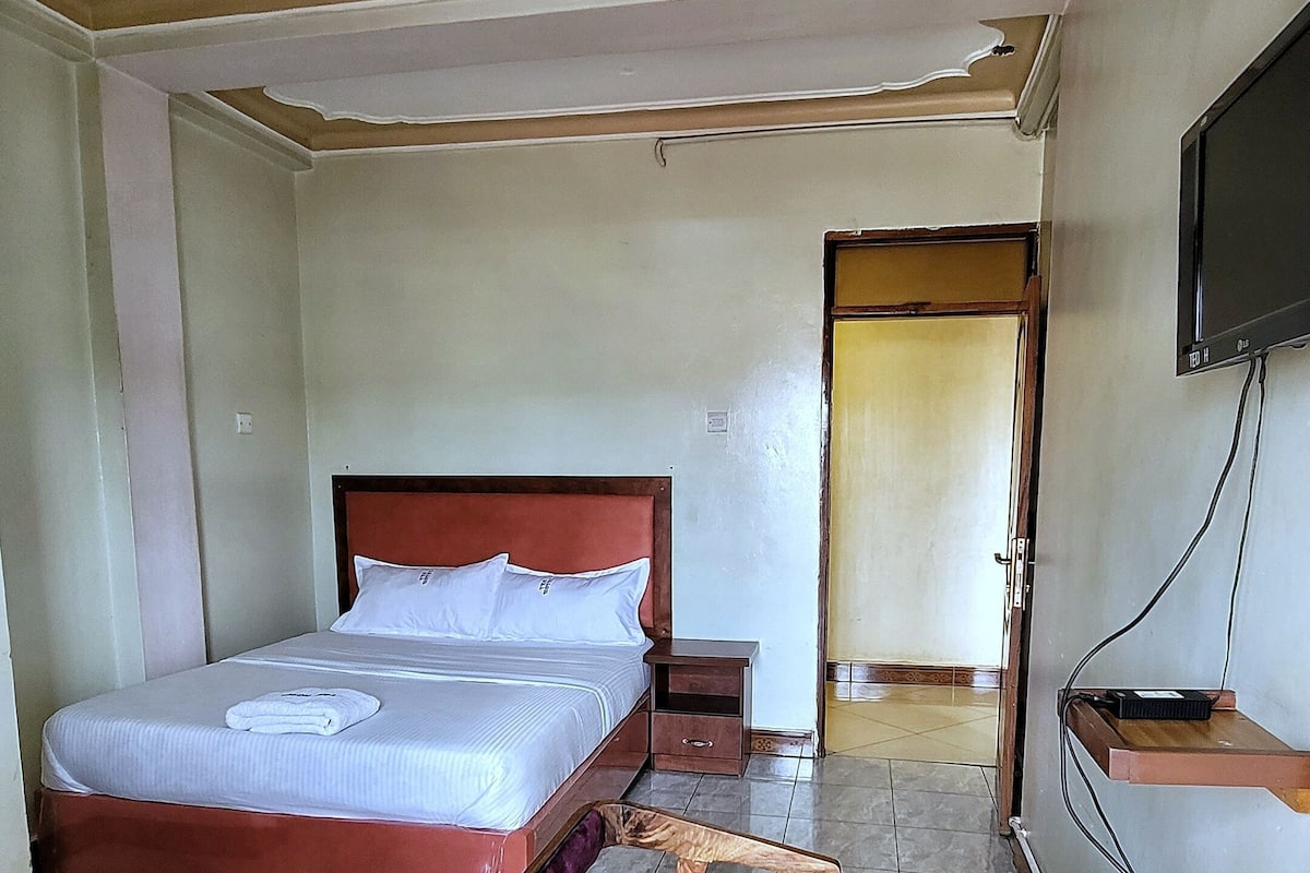 A hotel room with a bed, a wooden chair, a small table, and a television.