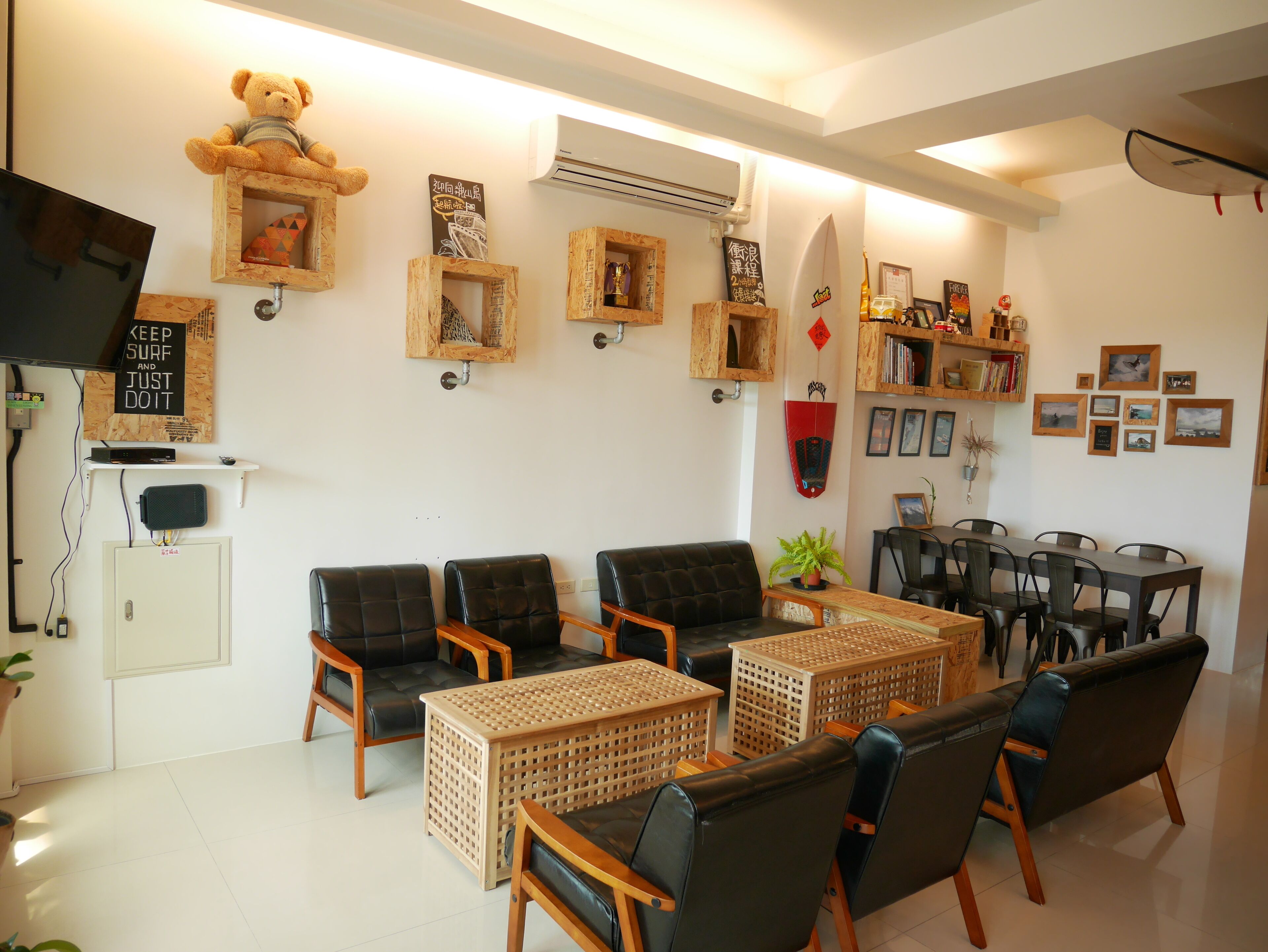 A cozy living room with a sofa, chairs, a coffee table, and a dining table. There are wall decorations, a teddy bear, and a TV.