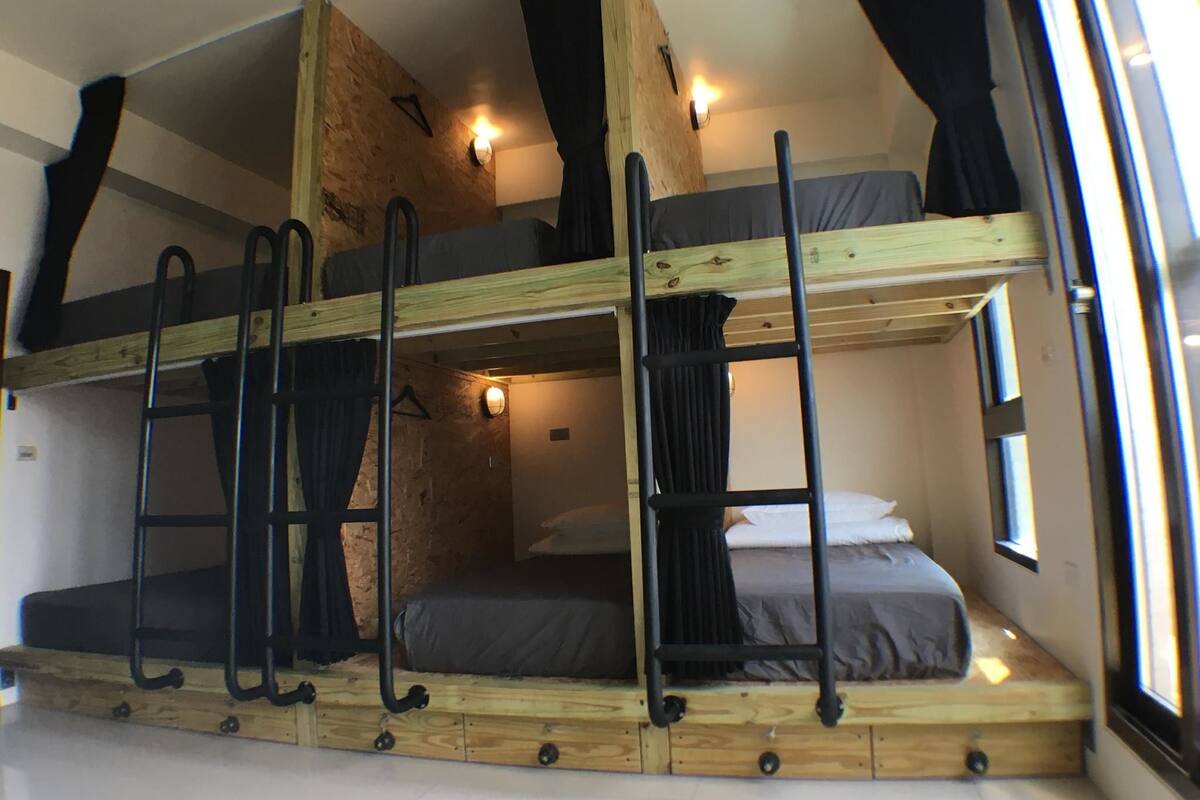 Habitación con literas, vigas de madera, una escalera y un ventanal.