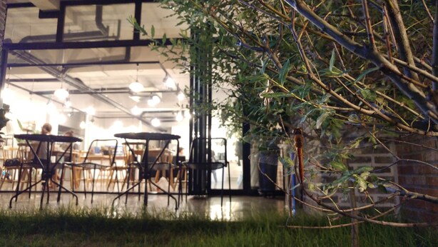 An indoor cafe with tables and chairs, a brick wall, and a hanging plant.