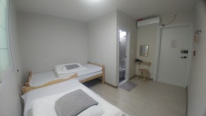 A small, clean room with two single beds, a wooden desk, a chair, a mirror, and a door with an air conditioning unit above it.