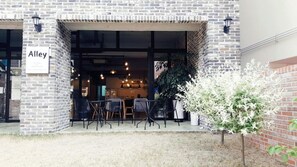 A brick building with a sign reading "Alley." Inside, there are tables and chairs arranged for dining.