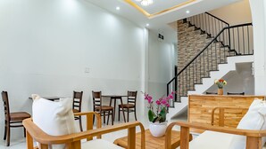 Un salon moderne avec un comptoir d’accueil en bois, un escalier agrémenté d’un mur en pierre et un coin repas avec des chaises et des tables en bois.