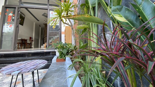 Un bâtiment moderne doté d’une entrée en verre, d’un patio avec une table et des chaises, et agrémenté de diverses plantes vertes.