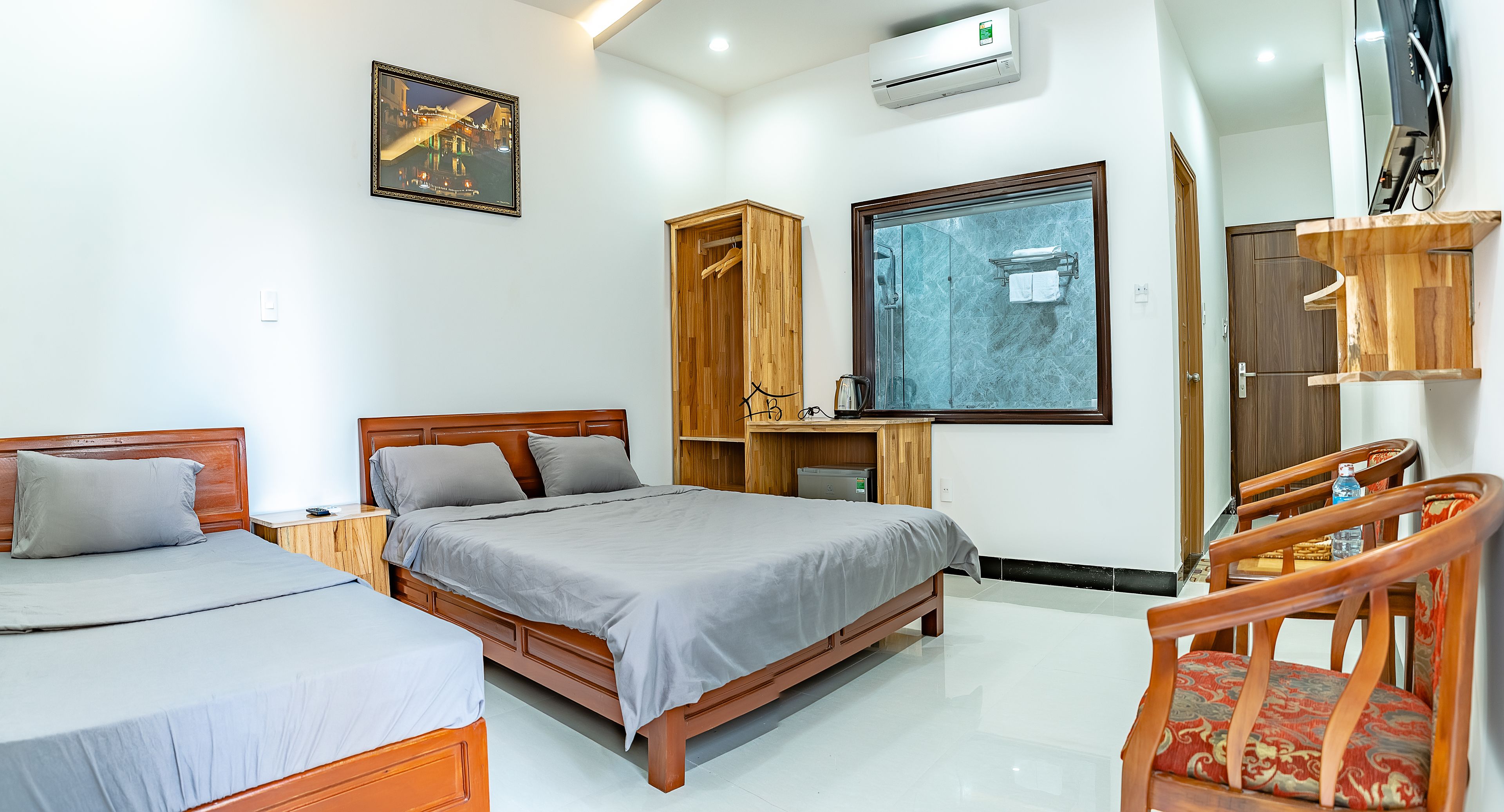A hotel room with two beds, a wooden wardrobe, a shower area, and a wooden chair.