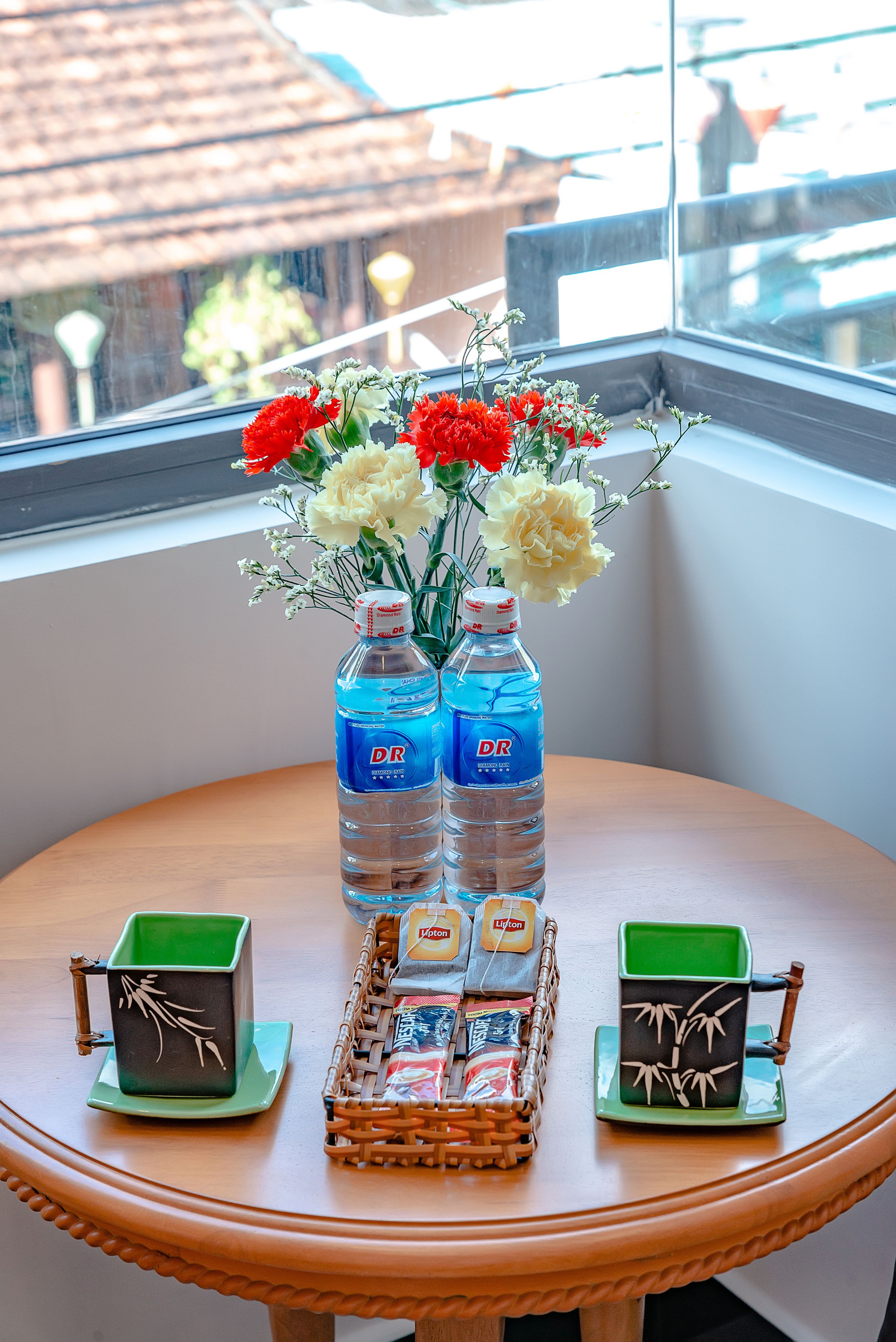 A table with a vase of flowers, two bottles of water, and two small baskets with tea bags and a green cup.