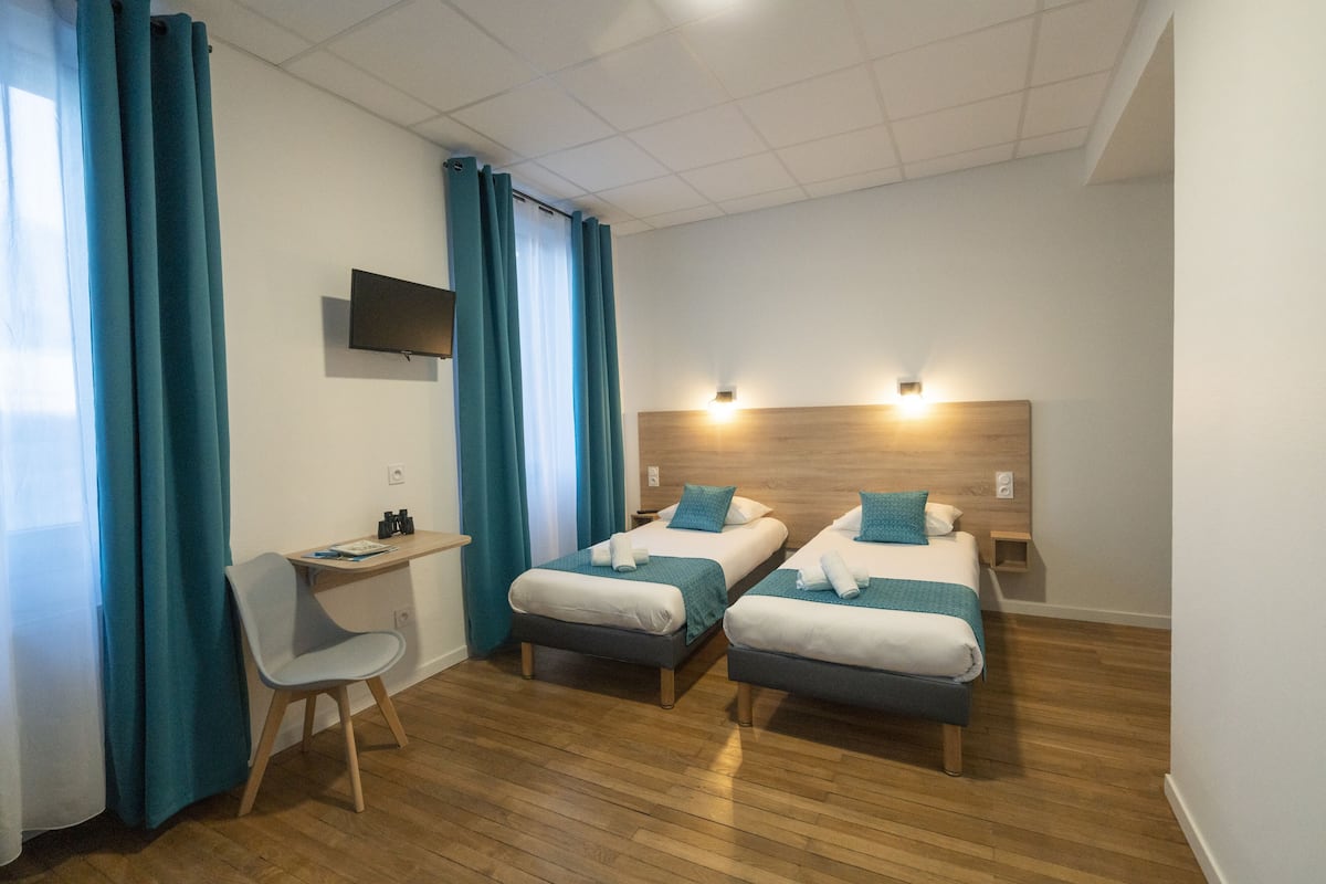 A hotel room with two single beds, a desk, a chair, and a TV mounted on the wall.