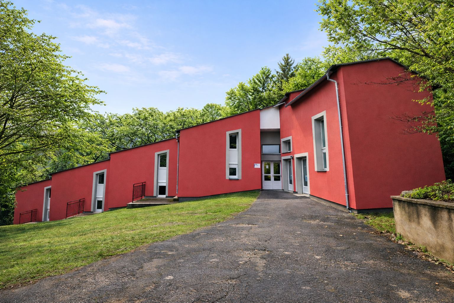 A red building with a central entrance, surrounded by greenery.