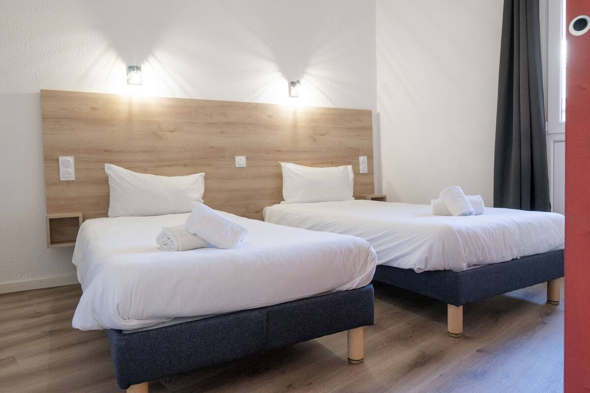 Two beds with wooden headboards, white bedding, and bedside lamps.