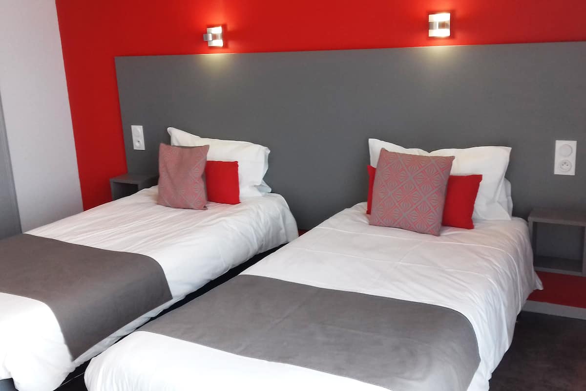 Two single beds with grey and white bedding, red and grey pillows, and a grey headboard.