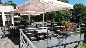 An outdoor dining area with tables and chairs, covered by umbrellas, and a metal railing. - La Petite Pierre - ULVF Vacances (La Petite-Pierre)