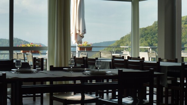 A restaurant with tables set for dining, large windows, and a view of a lake and hills. - La Petite Pierre - ULVF Vacances (La Petite-Pierre)