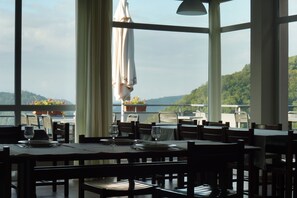 A restaurant with tables set for dining, large windows, and a view of a lake and hills. - La Petite Pierre - ULVF Vacances (La Petite-Pierre)