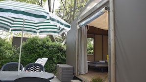 A small outdoor seating area with a table and chairs, a striped umbrella, and a tent entrance. - Camping U Libecciu  - Vacances ULVF (Calvi)
