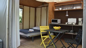 A compact room with a bed, a table with a bowl of fruit, a chair, a microwave, and a shelf with dishes. - Camping U Libecciu  - Vacances ULVF (Calvi)